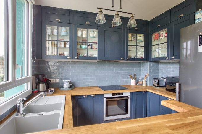 Cuisine rénovée avec façades bleues, plan de travail en chêne naturel, crédence en zelliges bleu-gris et vitrines avec pots vintage