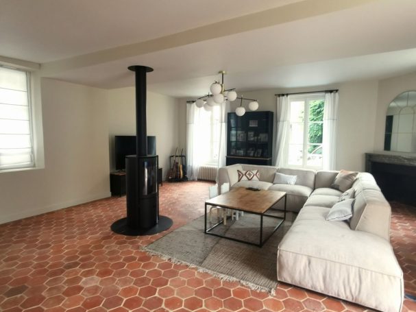 Salon rénové avec tomettes authentiques hexagonales, poêle à bois et grand canapé beige